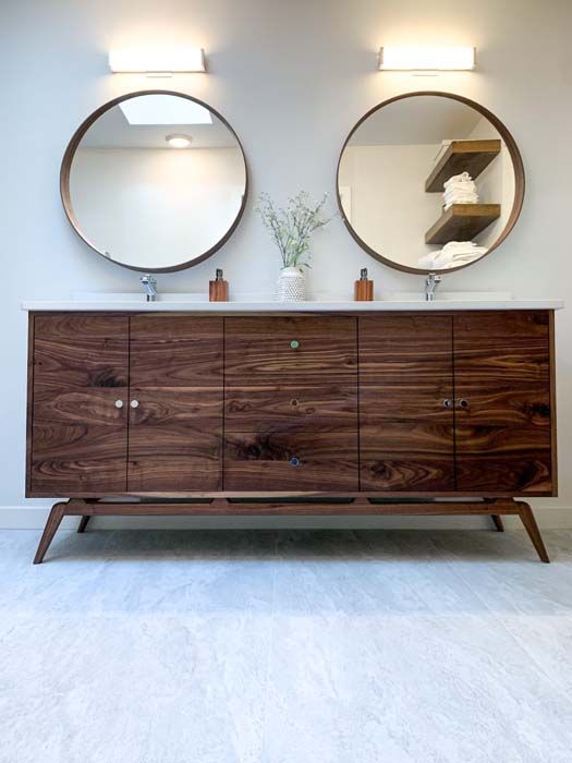 Mid-century modern bathroom vanity with a dark wood cabinet, two round mirrors, and overhead lighting.