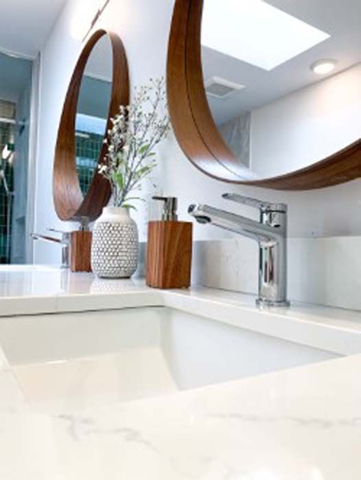White bathroom countertop with a sink, chrome faucet, and wooden-framed mirrors. A vase of white flowers sits on the counter.