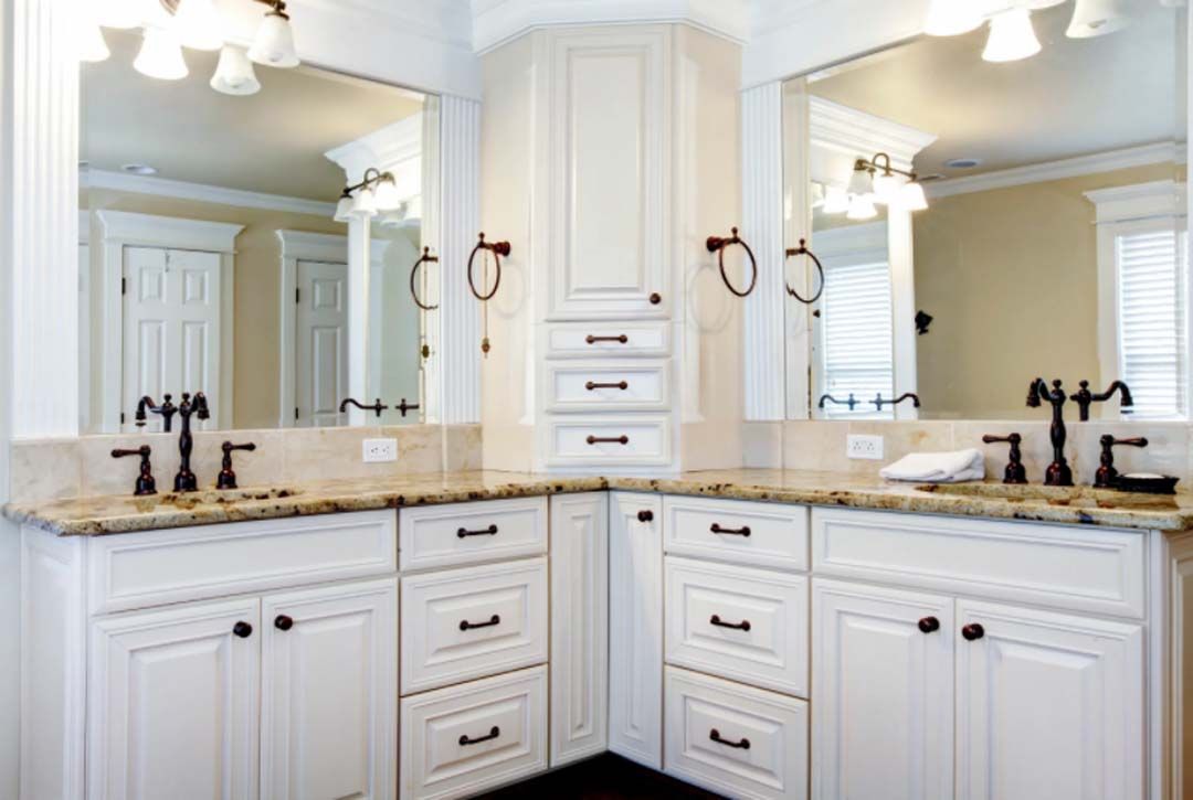 White bathroom vanity with two sinks, mirrors, and a central cabinet. Black fixtures and hardware, cream countertops, and pale walls.