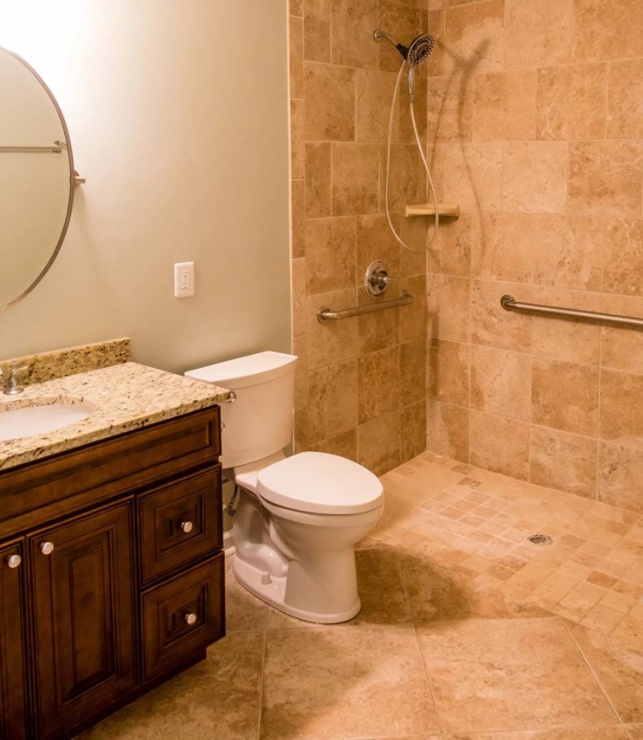 Accessible bathroom with a brown tile shower, toilet, and vanity. Features include grab bars, a roll-in shower, and a low vanity.