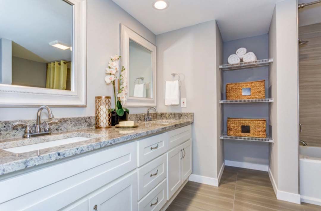A modern bathroom with a white vanity, granite countertop, and built-in shelves holding baskets and towels.
