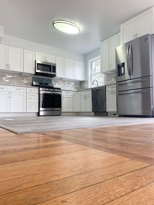 A newly renovated kitchen with white cabinets, stainless steel appliances, and wood flooring. The kitchen is well-lit and appears modern.