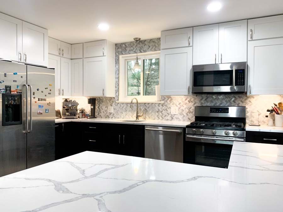 Modern kitchen with white upper cabinets, black lower cabinets, stainless steel appliances, and a white marble countertop.