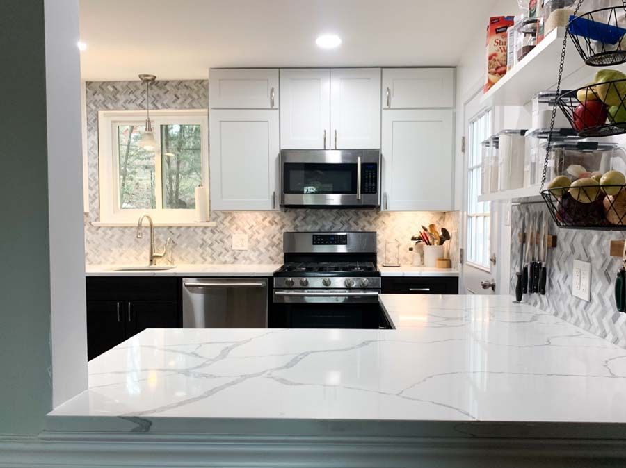 Modern kitchen with white upper cabinets, black lower cabinets, stainless steel appliances, and a white countertop with marble-like veining.