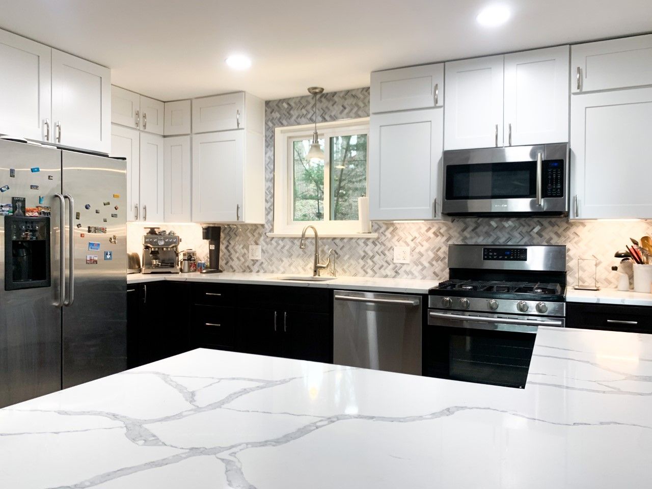 Modern kitchen with white upper cabinets, black lower cabinets, stainless steel appliances, and a white countertop with gray veining.