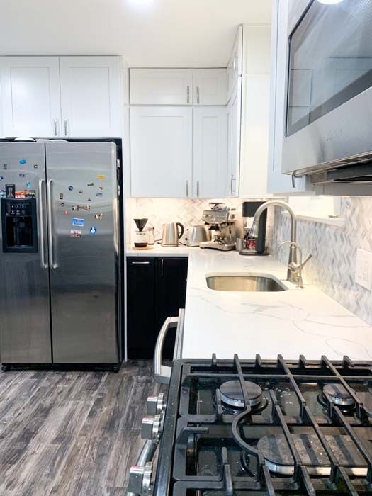 A modern kitchen with stainless steel appliances, white cabinets, and marble countertops. The foreground shows a black gas stove.