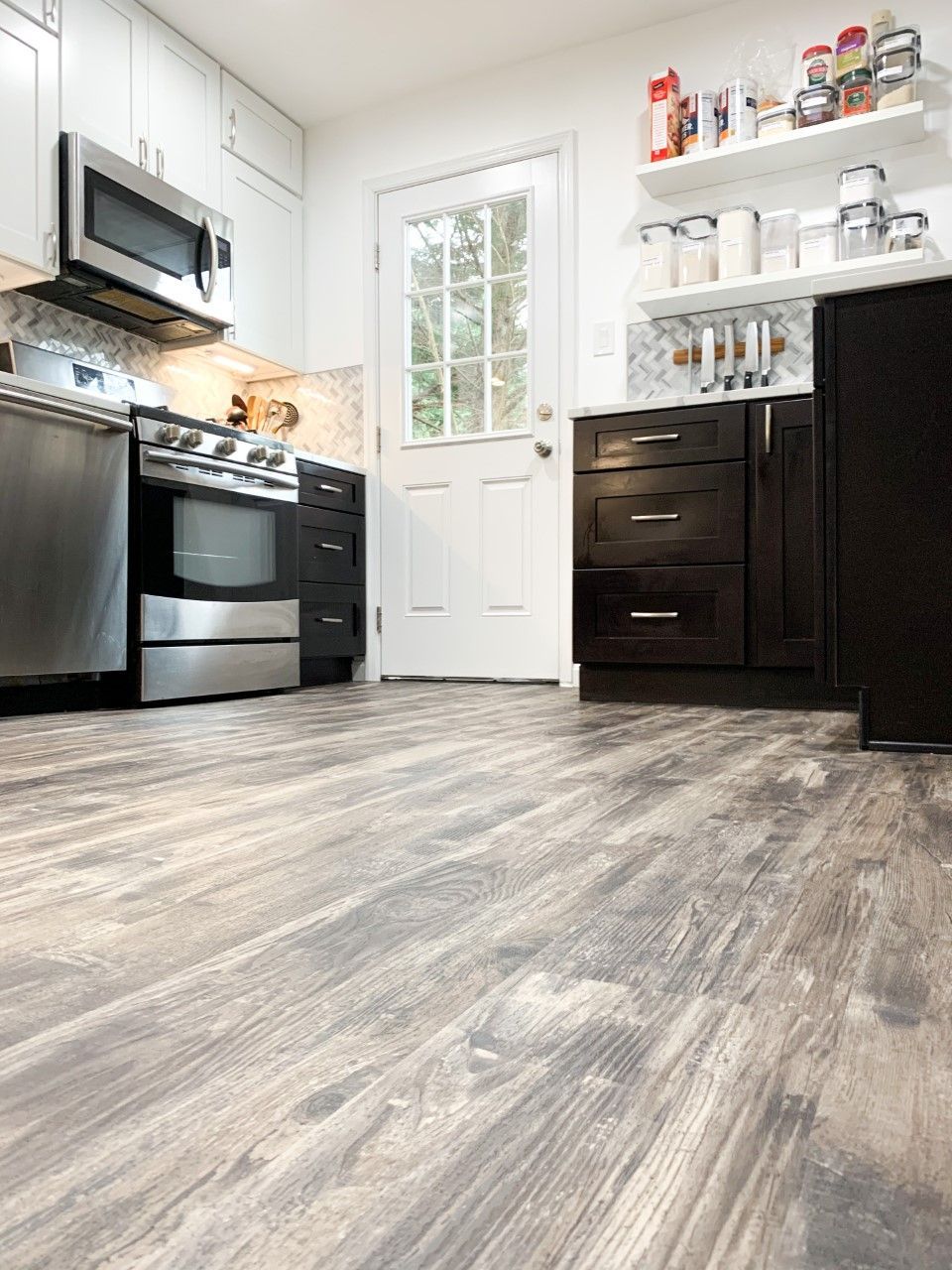 Kitchen with dark wood cabinets, stainless steel appliances, white door, and light wood-look flooring.