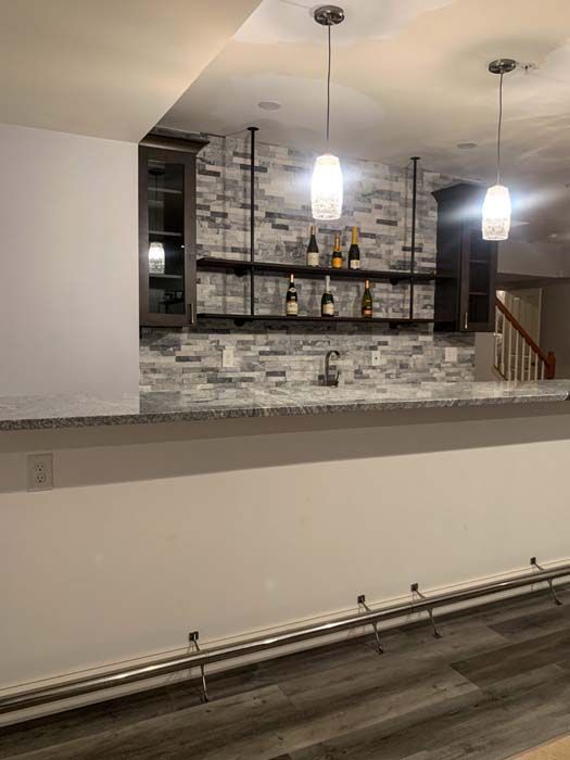 A newly built bar with a gray countertop, brick backsplash, and shelves with bottles. Two pendant lights hang above.