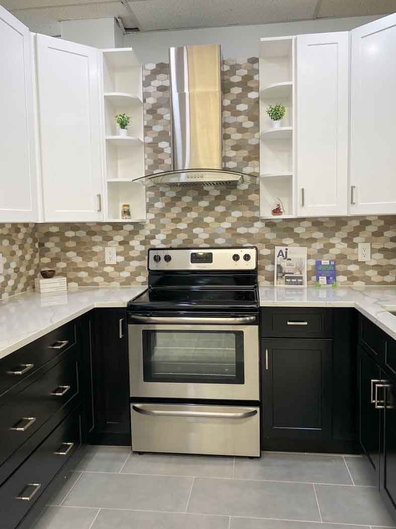 U-shaped kitchen with white upper cabinets and black lower cabinets. Stainless steel oven sits against a mosaic backsplash.