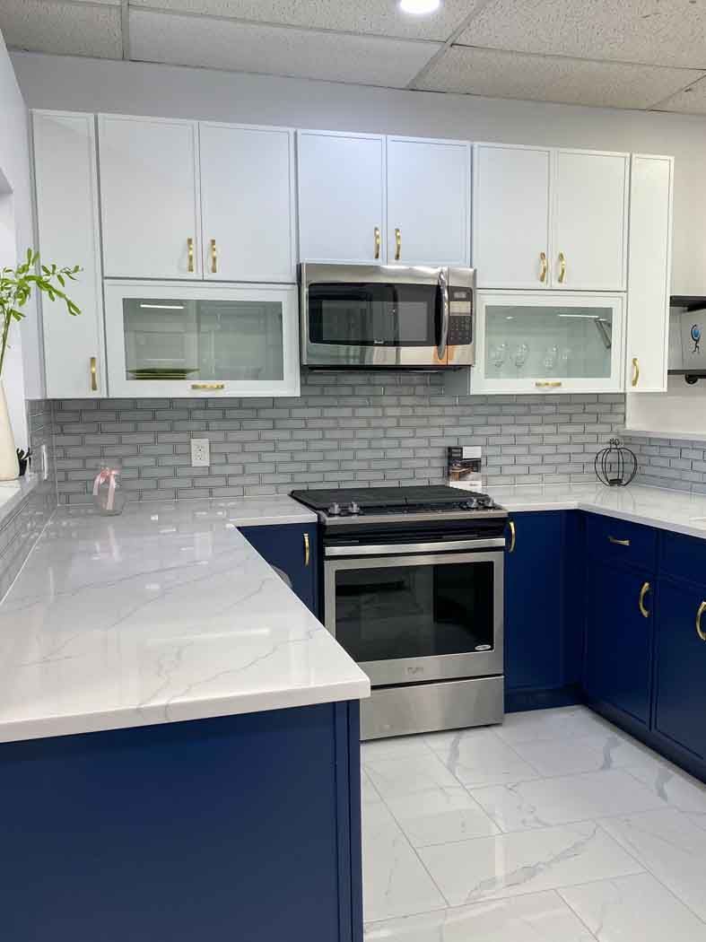 A modern kitchen with white and blue cabinets, a stainless steel oven and microwave, and white countertops.