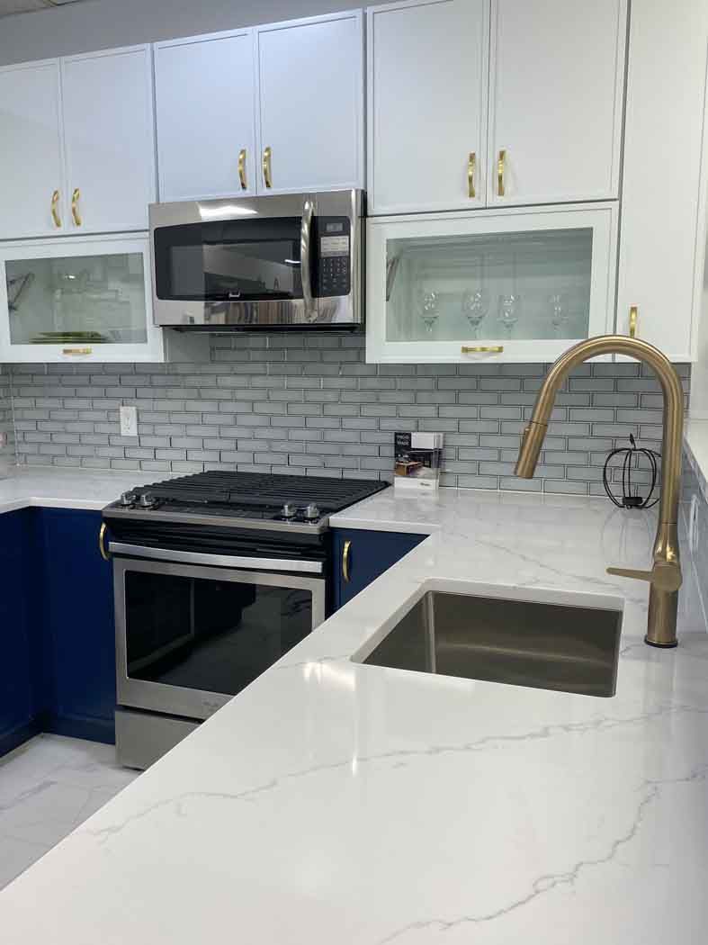 Kitchen with white countertops, stainless steel appliances, white and blue cabinets, and a gold faucet.