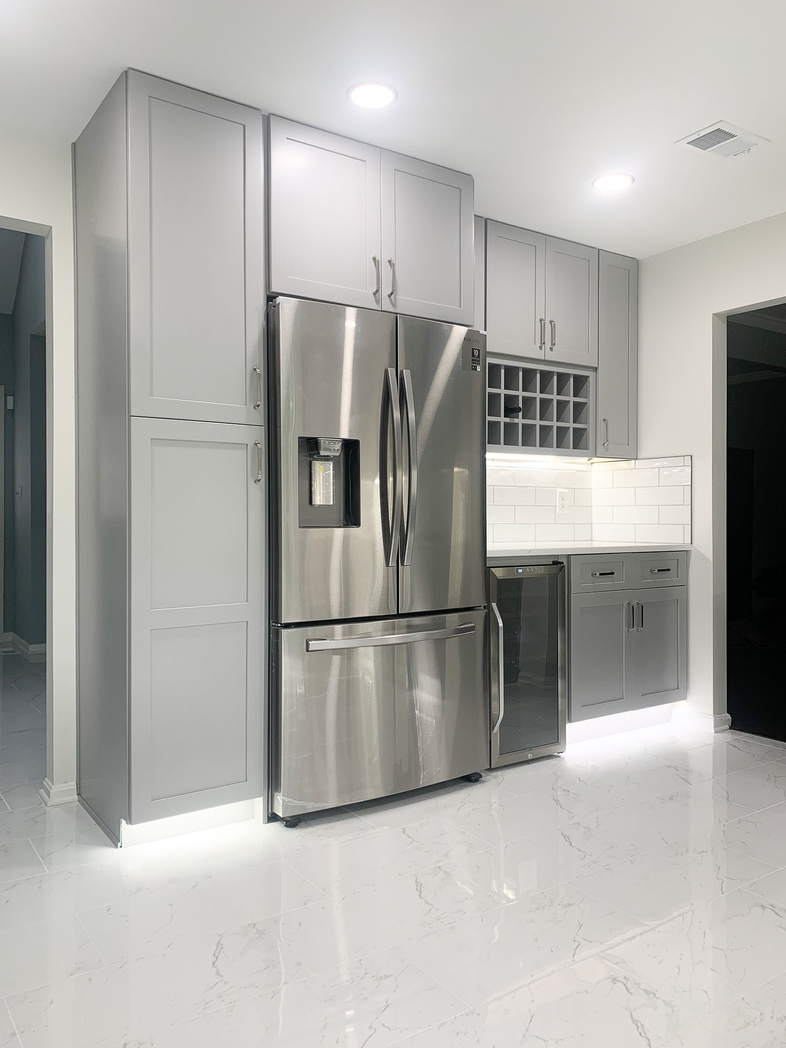 Modern kitchen with gray cabinets and stainless steel refrigerator. White floor with under-cabinet lighting.