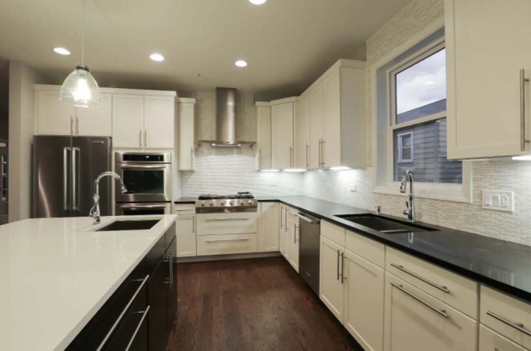 Modern kitchen with white cabinets, dark countertops, stainless steel appliances, and a large island.