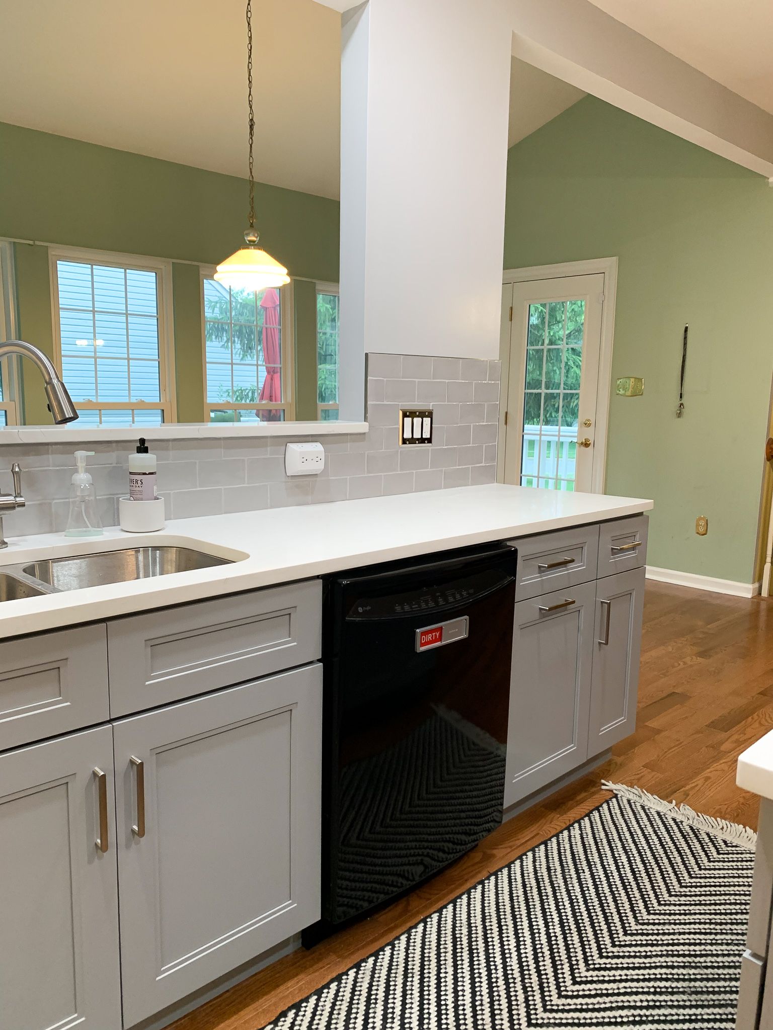 Kitchen with gray cabinets, a black dishwasher, white countertop, and a black and white rug.