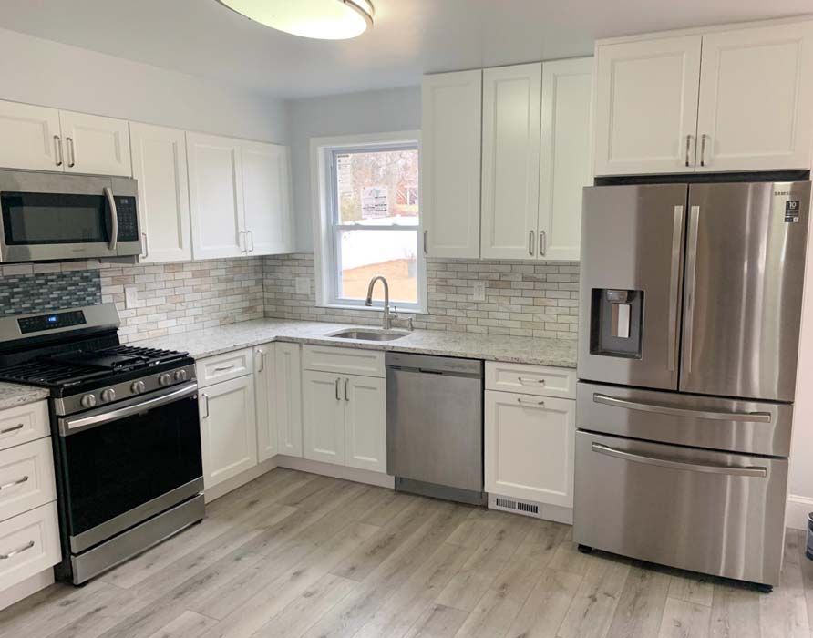 A modern, white kitchen with stainless steel appliances and light gray flooring. Features a gas range, refrigerator, and sink.