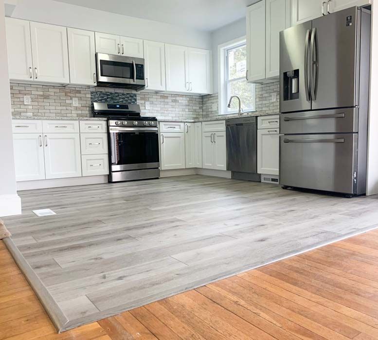 A modern kitchen with white cabinets, stainless steel appliances, light gray flooring, and a light gray brick backsplash.