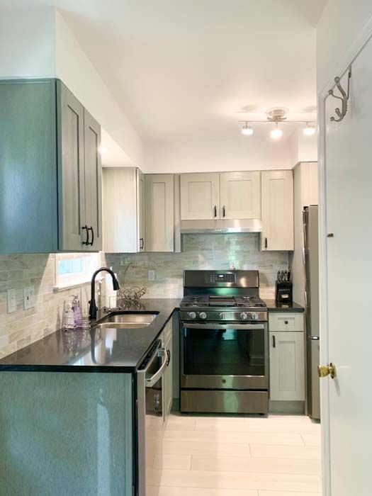 A modern kitchen with gray cabinets, a black countertop, and stainless steel appliances. White tiled floor and light gray backsplash complete the design.