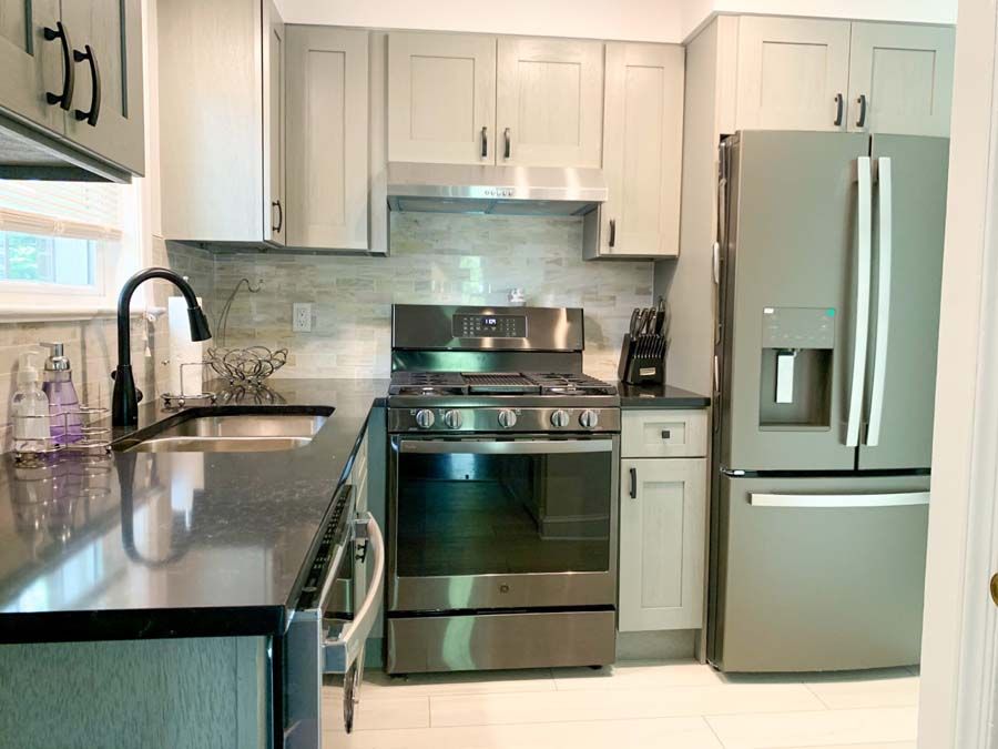Gray kitchen with stainless steel appliances, including a refrigerator, stove, and sink. Gray cabinets and black countertops are present.