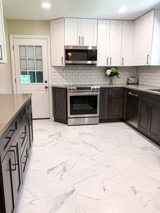 Modern kitchen with white and dark gray cabinets, stainless steel appliances, white marble-look flooring, and subway tile backsplash.