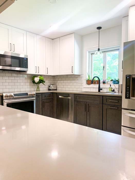 Modern kitchen with white upper cabinets, dark brown lower cabinets, stainless steel appliances, and a white countertop.