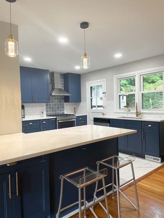 Navy blue kitchen with white countertops, island, and stools; gold-toned light fixtures.