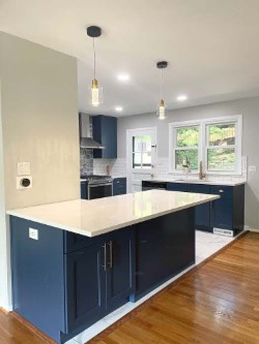 Modern kitchen with navy blue cabinets, white countertops, and wood flooring. Two pendant lights hang over the island.