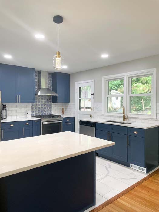 Blue kitchen with white countertops and tile. A light fixture hangs above the kitchen island.