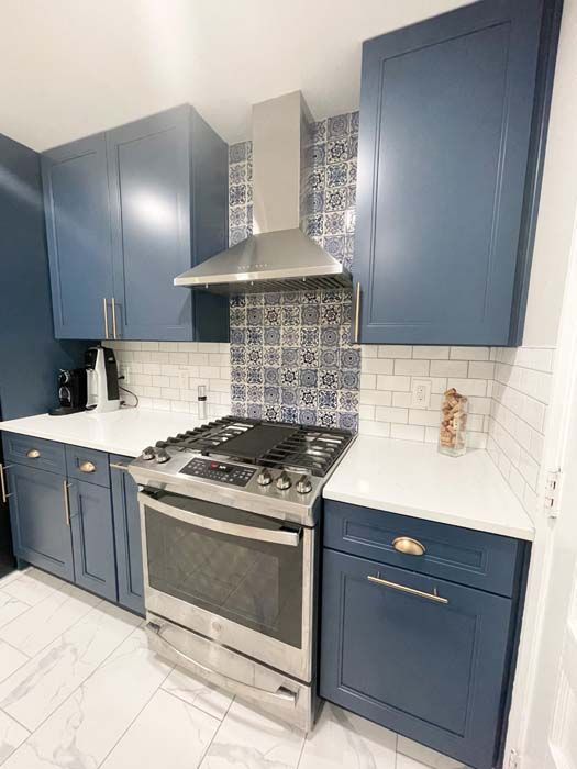 Blue kitchen with white countertops, stainless steel appliances, and patterned tile backsplash.
