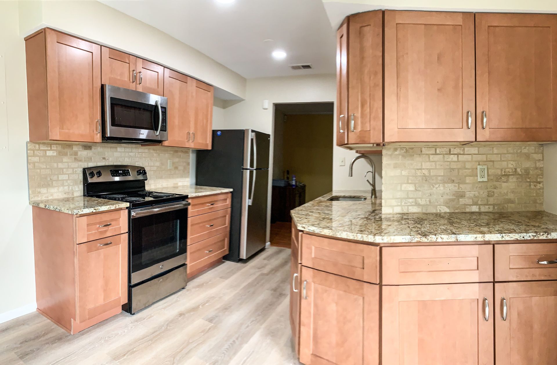 A kitchen featuring light brown cabinets, granite countertops, and stainless steel appliances against a beige tiled backsplash.