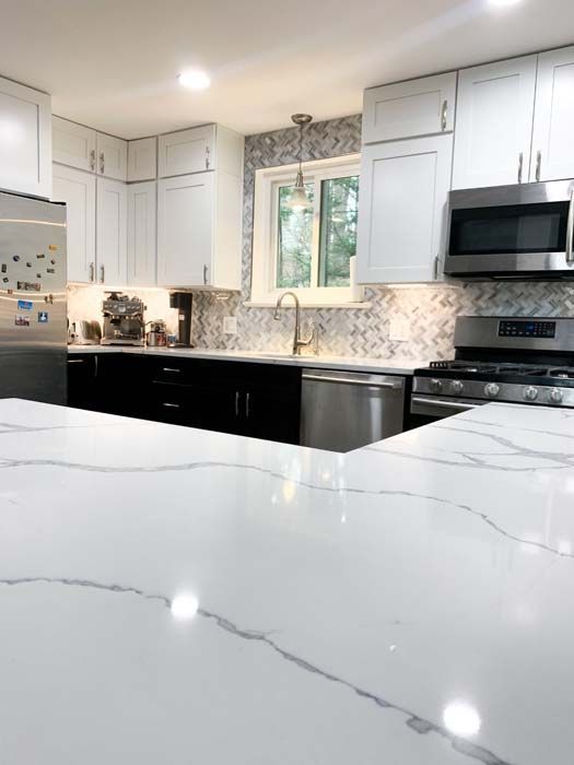 Modern kitchen with white cabinets, black lower cabinets, stainless steel appliances, and a marble countertop.