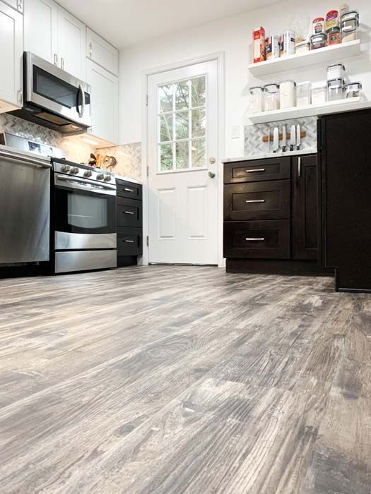 Kitchen with wood-look flooring, white cabinets, black lower cabinets, stainless steel appliances, and a white door.