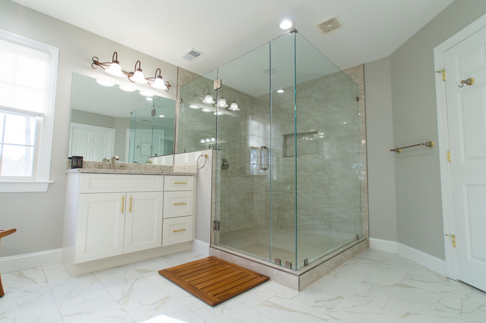 Bathroom with a large glass shower, white vanity, and marble floor; neutral color scheme.