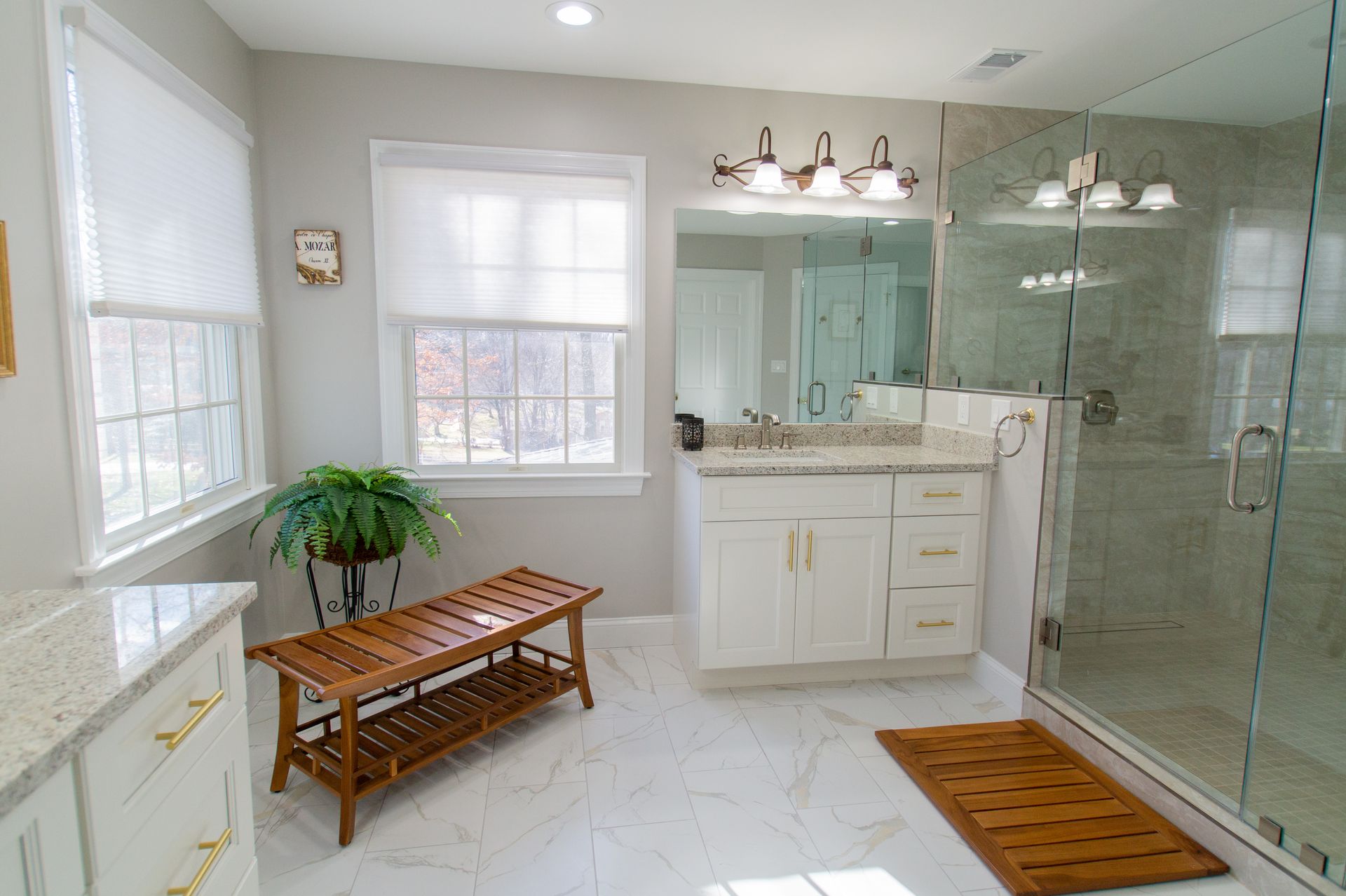 Bright bathroom with white cabinets, glass shower, and wooden accents. Soft light floods the space with a bench and plant.