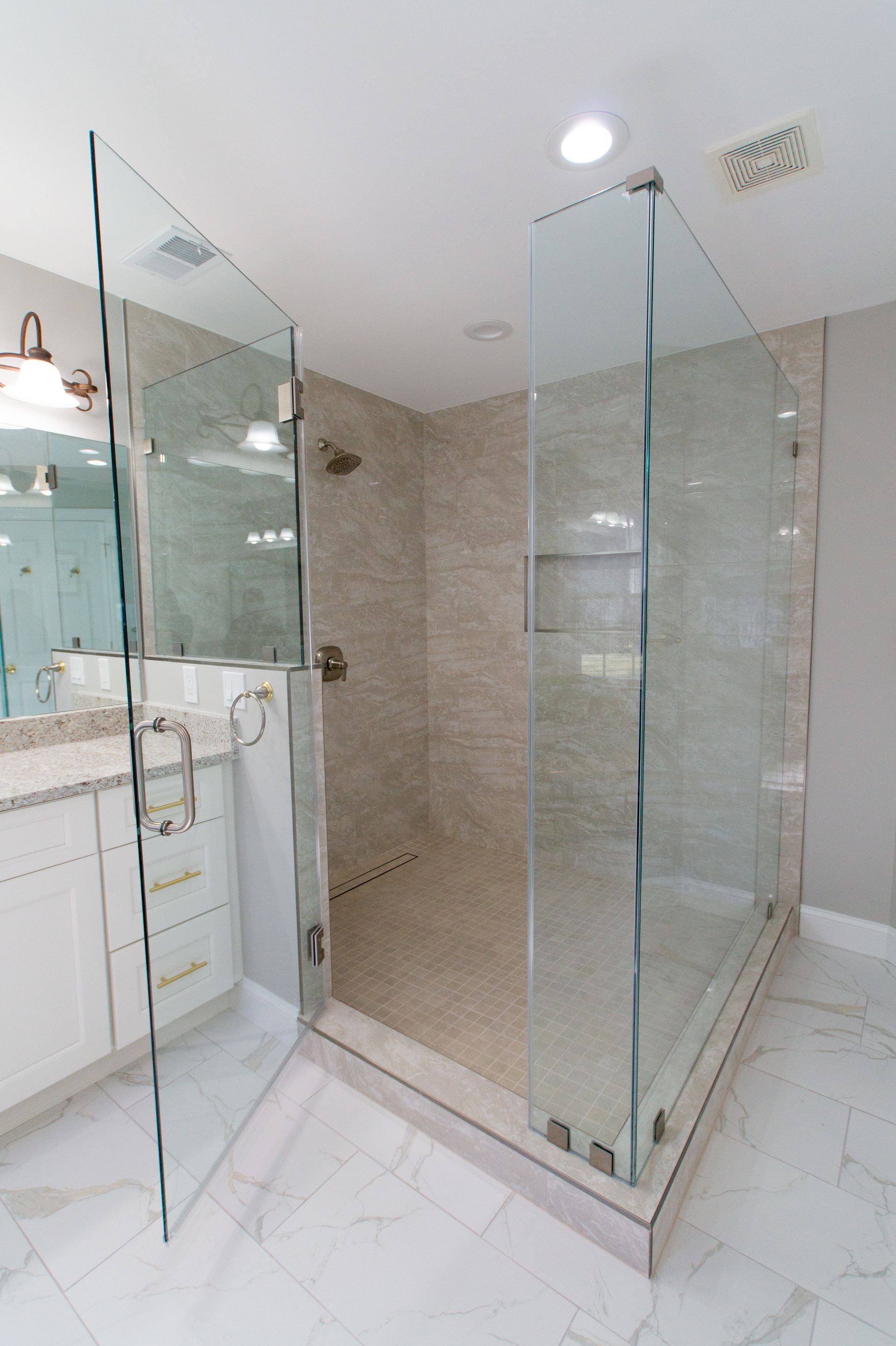 Modern bathroom with a large glass shower enclosure and marble flooring. The shower has a tiled interior and chrome fixtures.