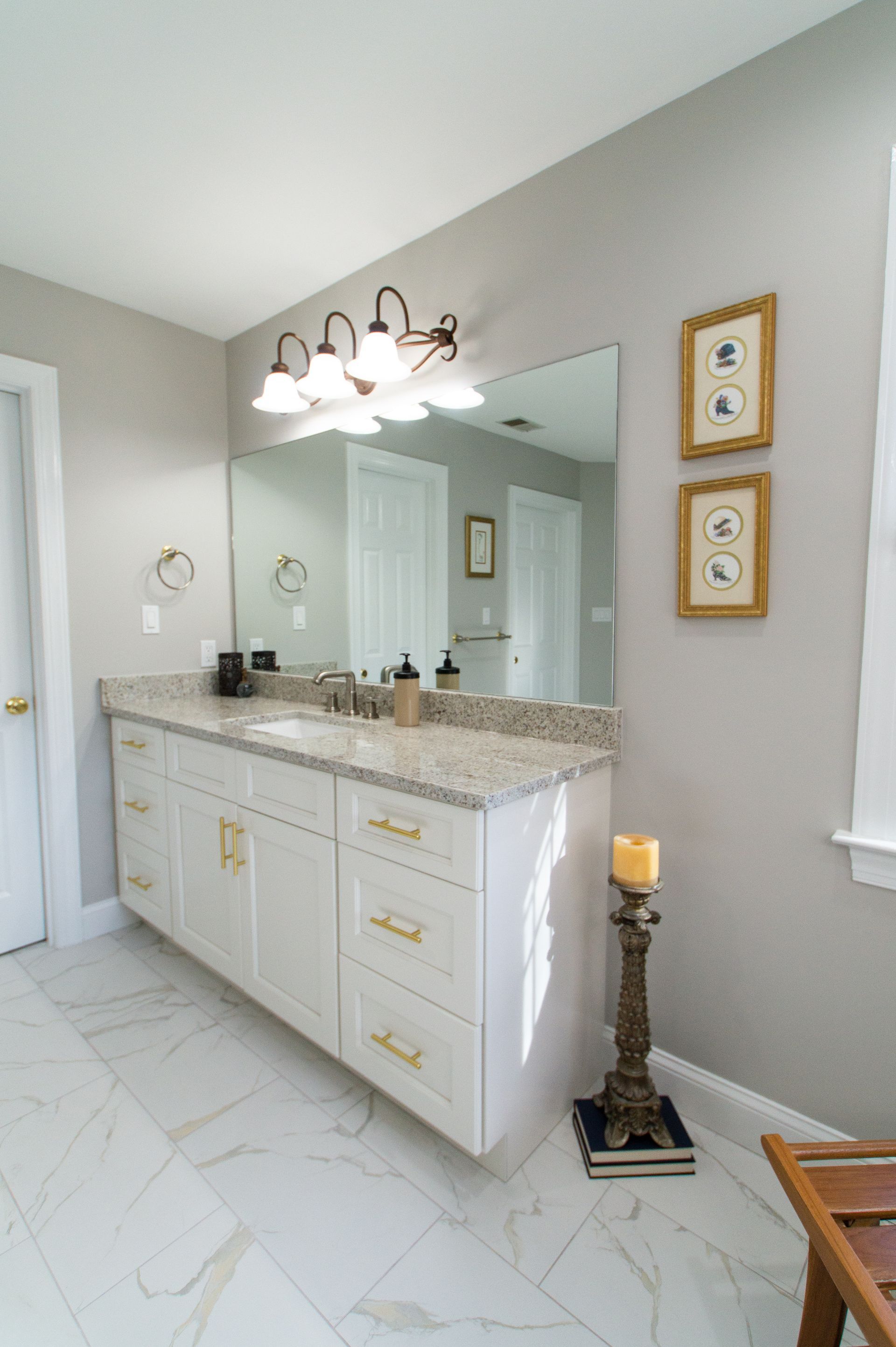 A modern bathroom with white cabinets, a gray countertop, and a large mirror, featuring a candle holder and gold accents.