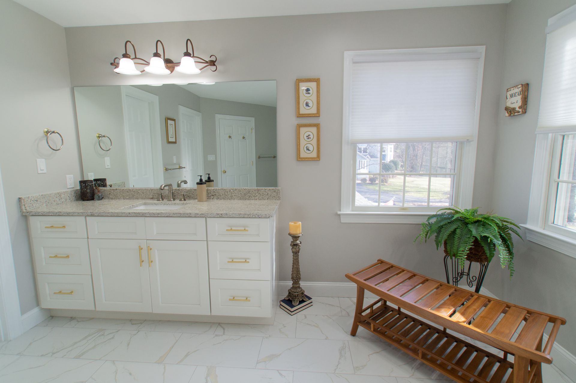 White bathroom with a vanity, window, and a wooden bench. The walls are gray, and the floor is tiled.