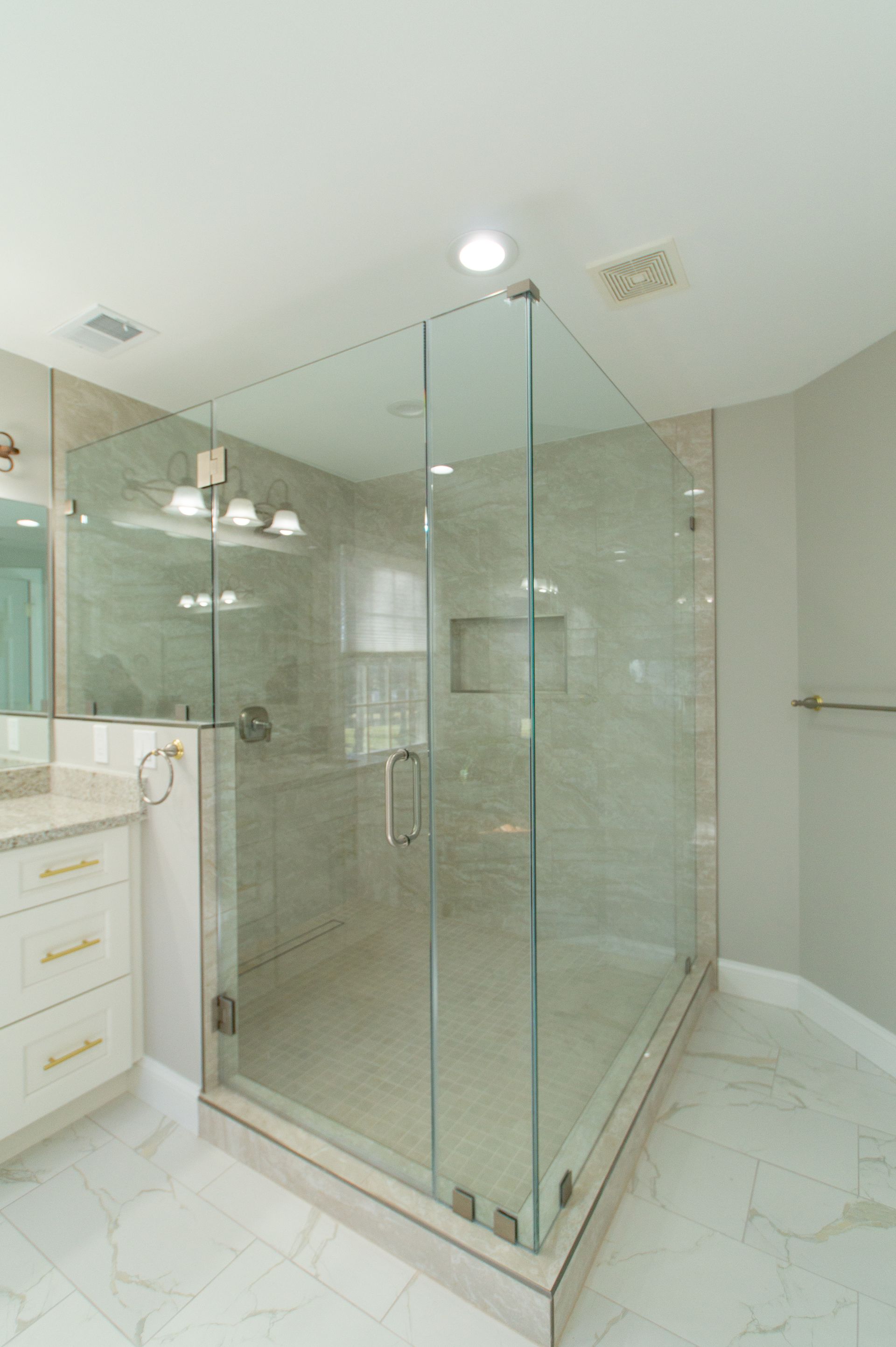 A spacious, modern bathroom features a large glass-enclosed shower with light gray tiling and marble floors.