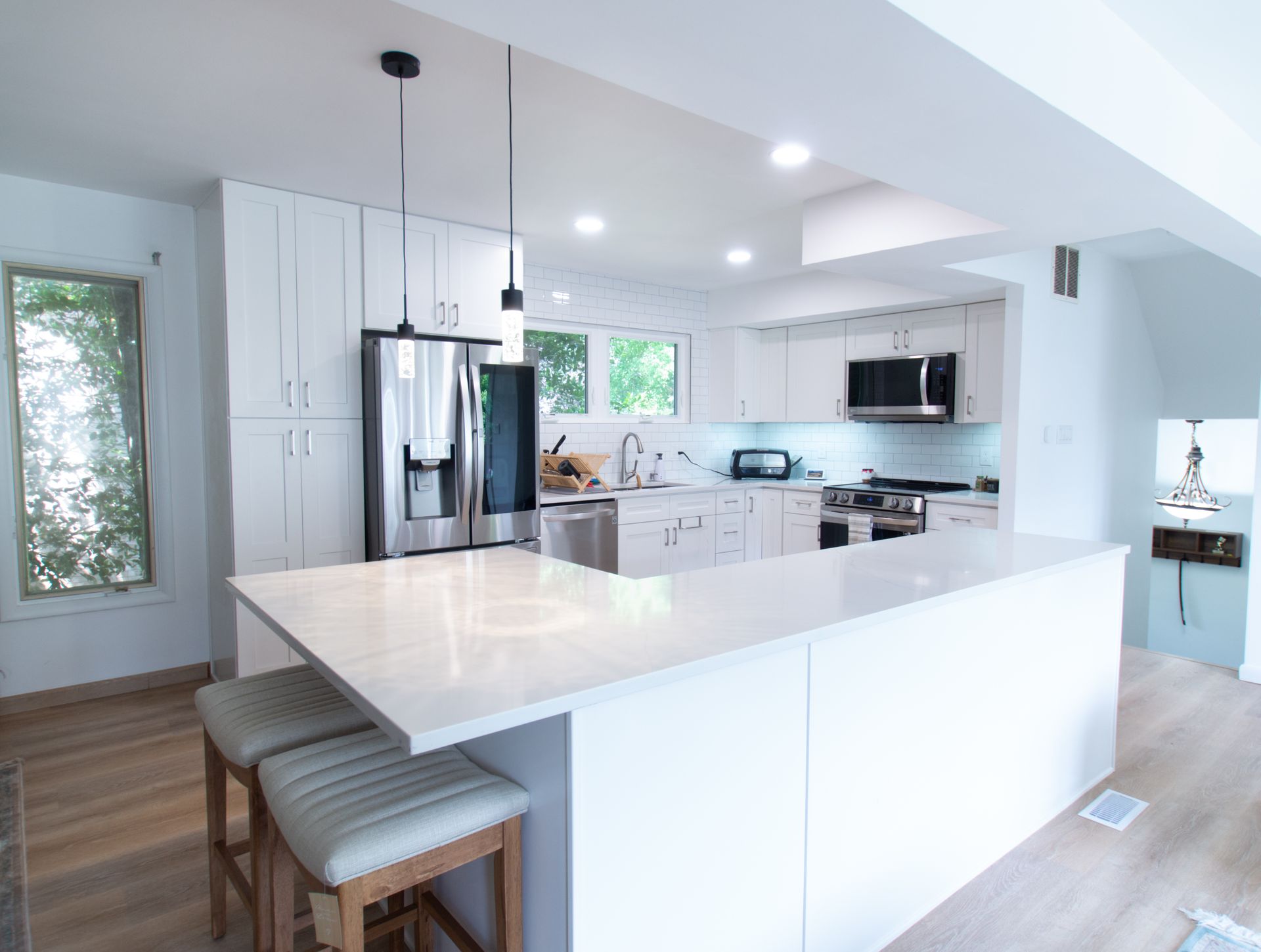 Modern, bright white kitchen with island, stainless steel appliances, and three bar stools.