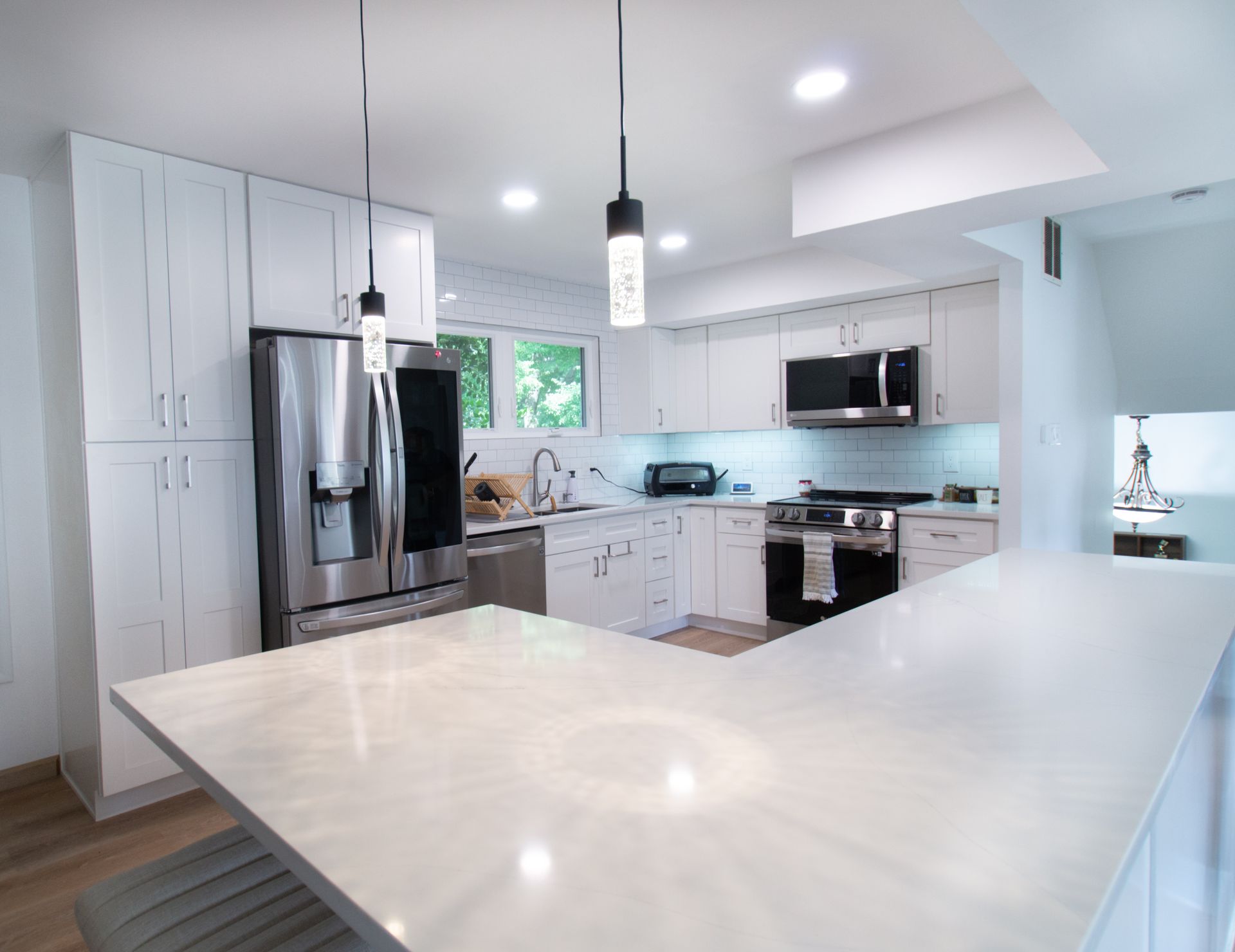 Modern white kitchen with stainless steel appliances, a large countertop, and pendant lights.