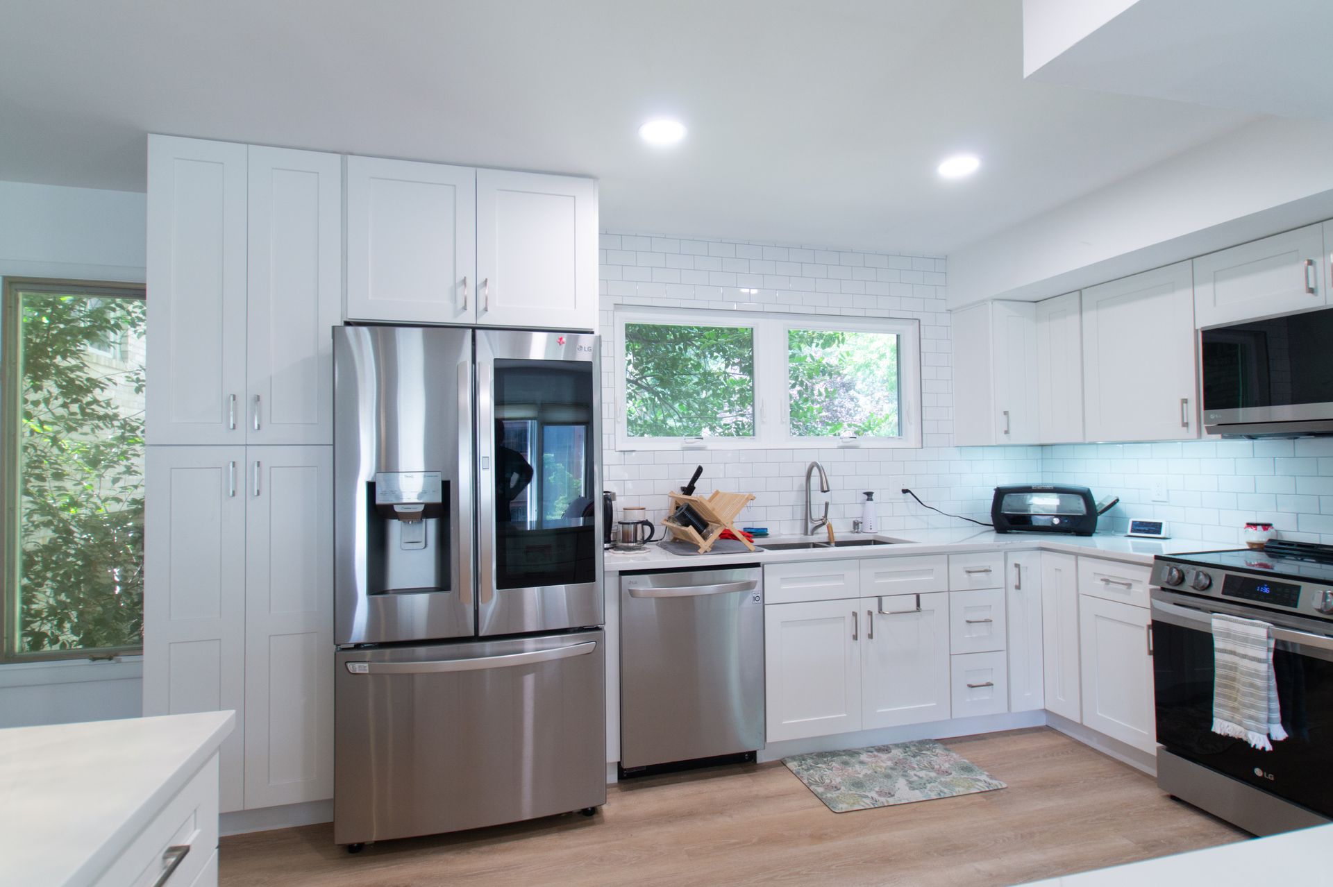 Bright, modern kitchen with white cabinets, stainless steel appliances, and a window overlooking greenery.