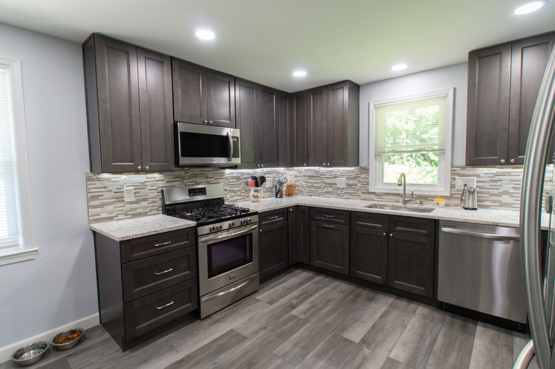 Modern kitchen with dark gray cabinets, stainless steel appliances, light gray countertops, and a wood-look floor.