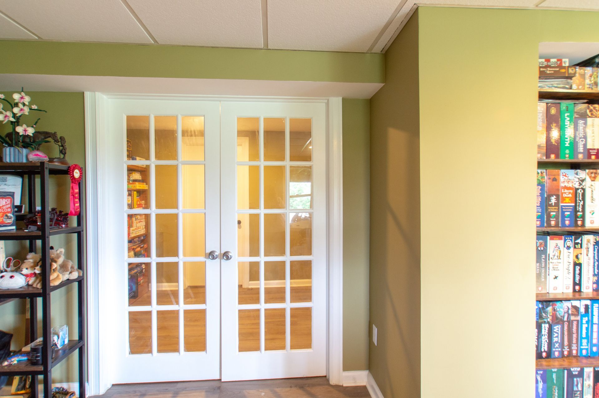 French doors leading into a room with shelves on the left and a bookcase on the right, painted with shades of green and brown.
