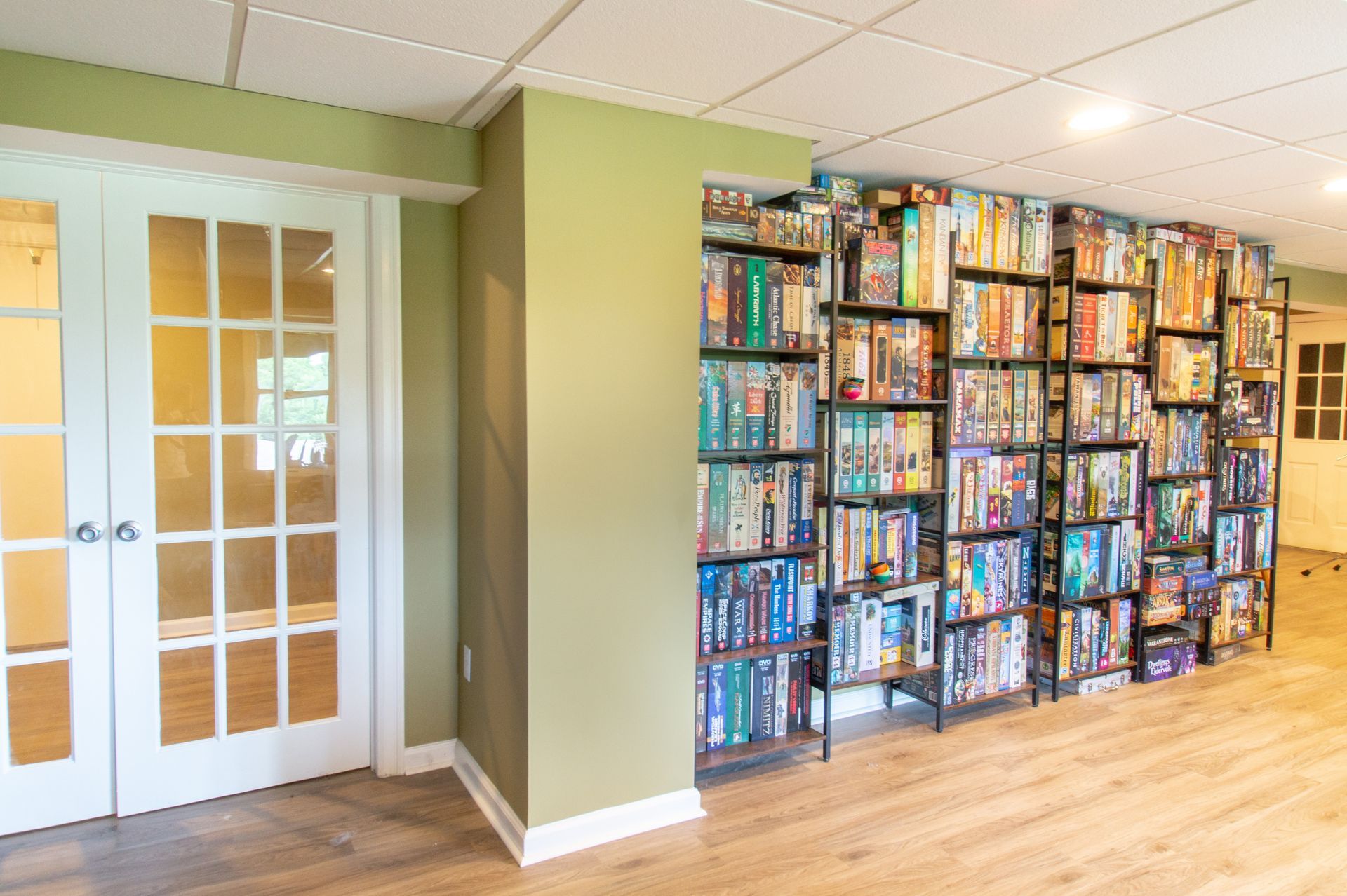 A room featuring a wall of shelves filled with DVDs. Adjacent is a doorway with glass panels and white doors.