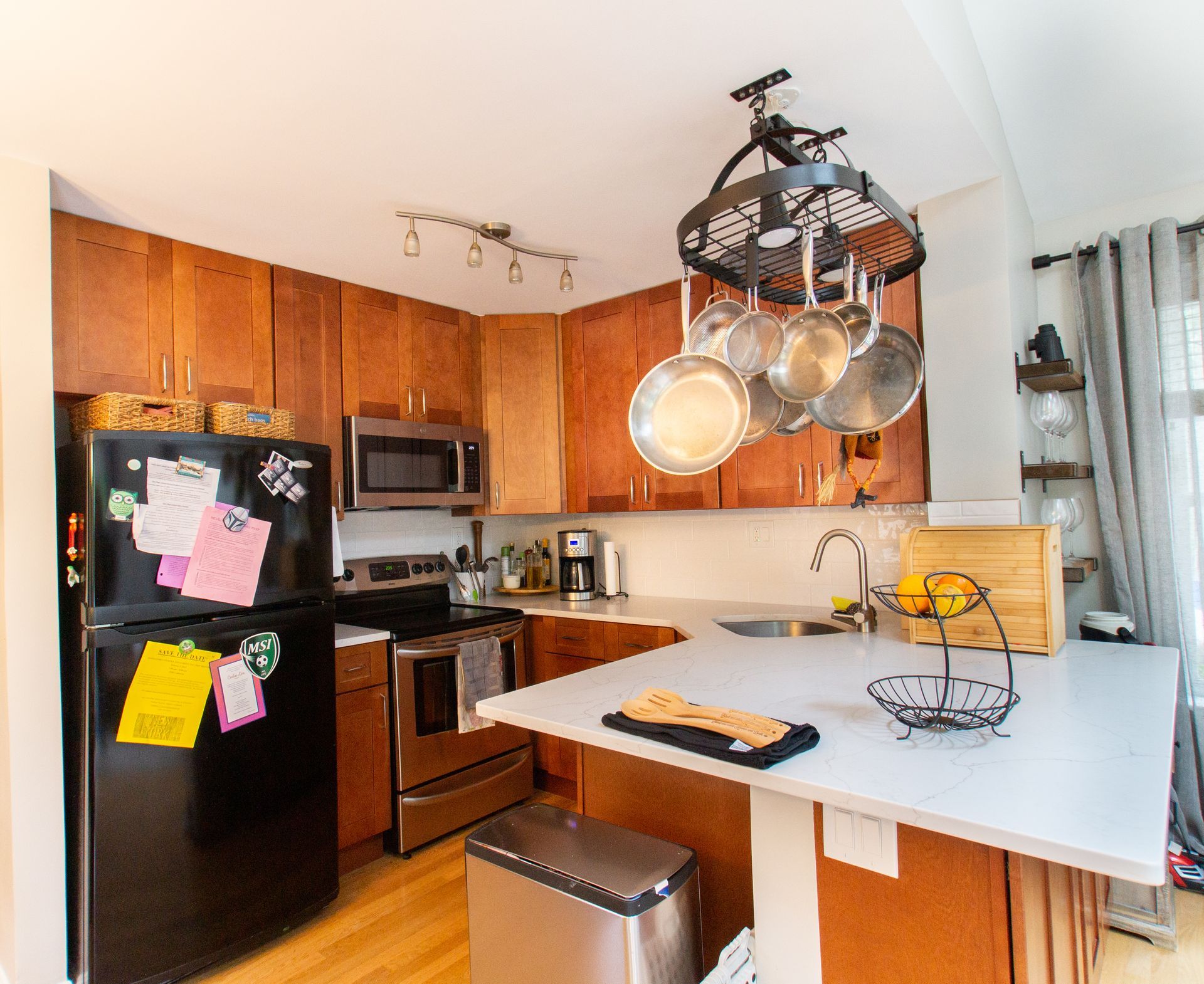 A kitchen with brown cabinets, stainless steel appliances, and a white countertop island. Pots hang from a rack above the island.