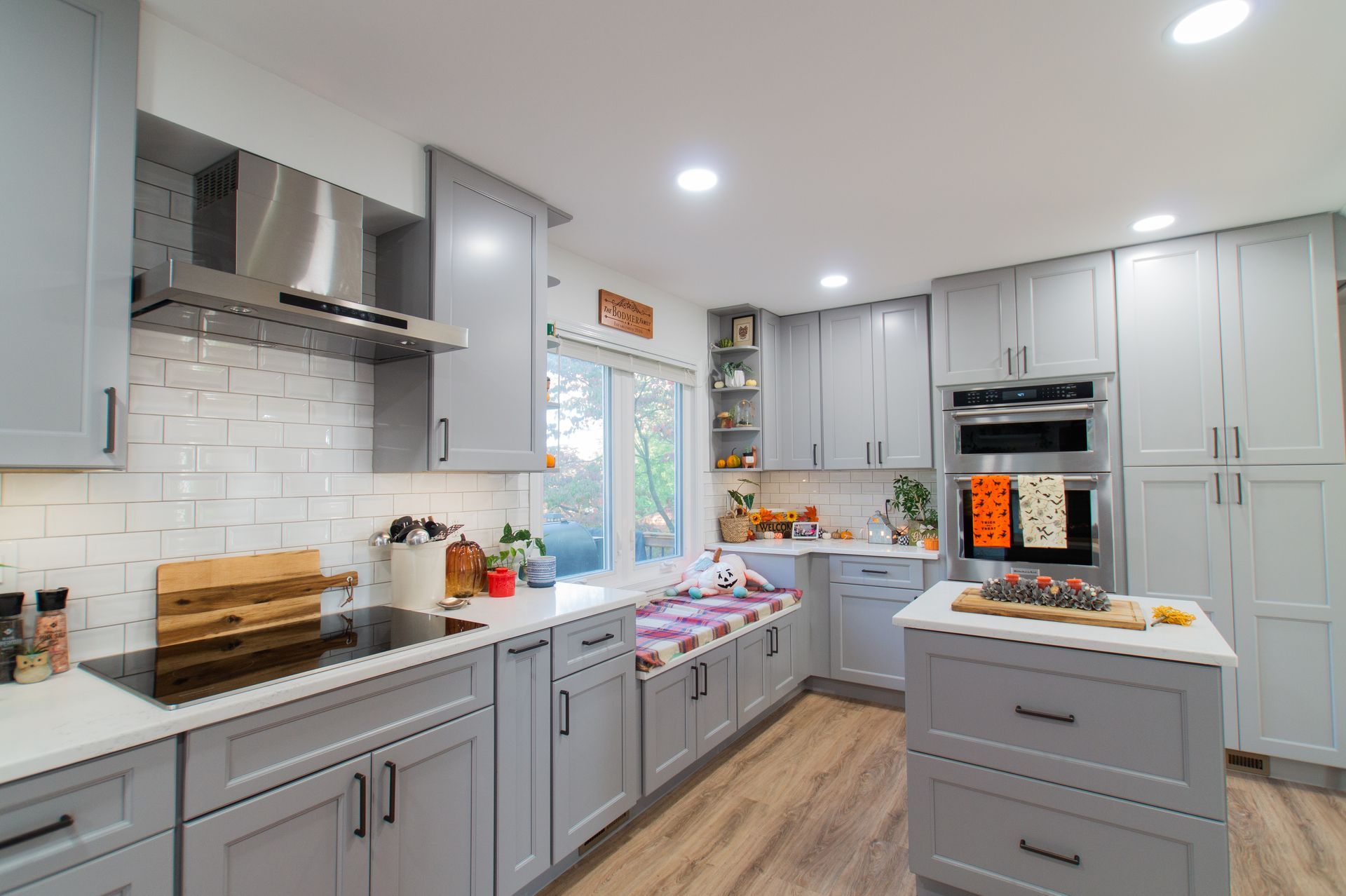 Gray kitchen with light wood floors. Features cabinets, stainless steel hood, and a built-in bench seat near a window.