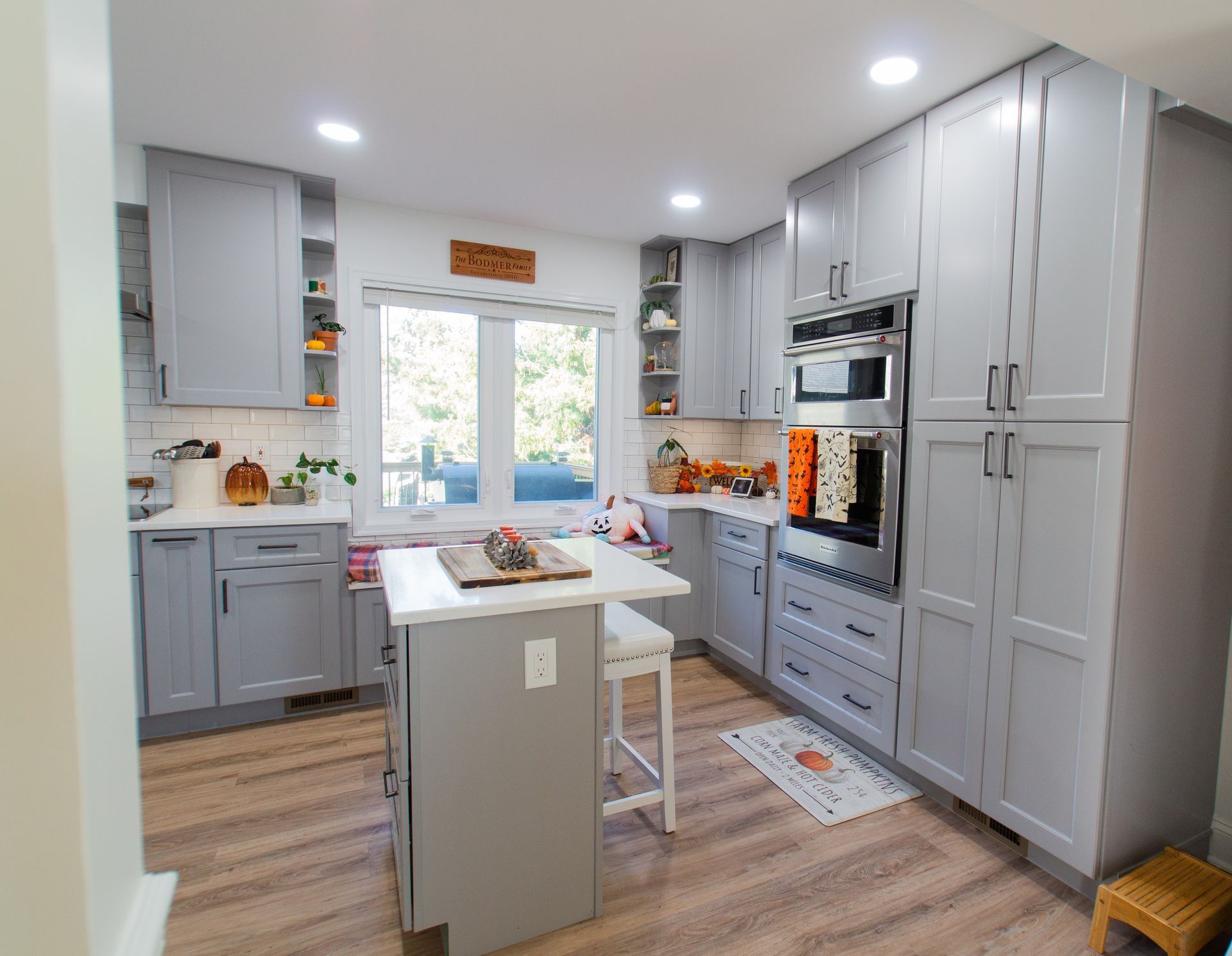 Light gray kitchen with wooden floors, cabinets, and an island. A window with natural light and fall decor is visible.