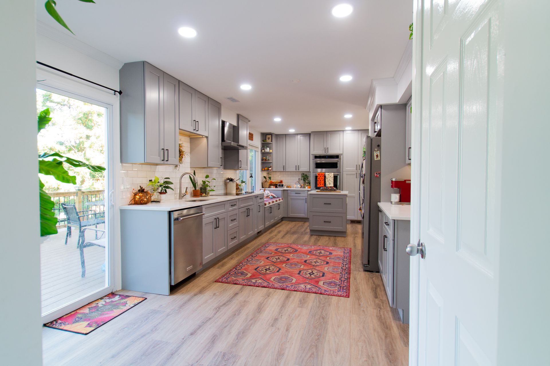 Spacious gray kitchen with light wood floors, white countertops, and a colorful rug. A door leads to an outdoor patio.