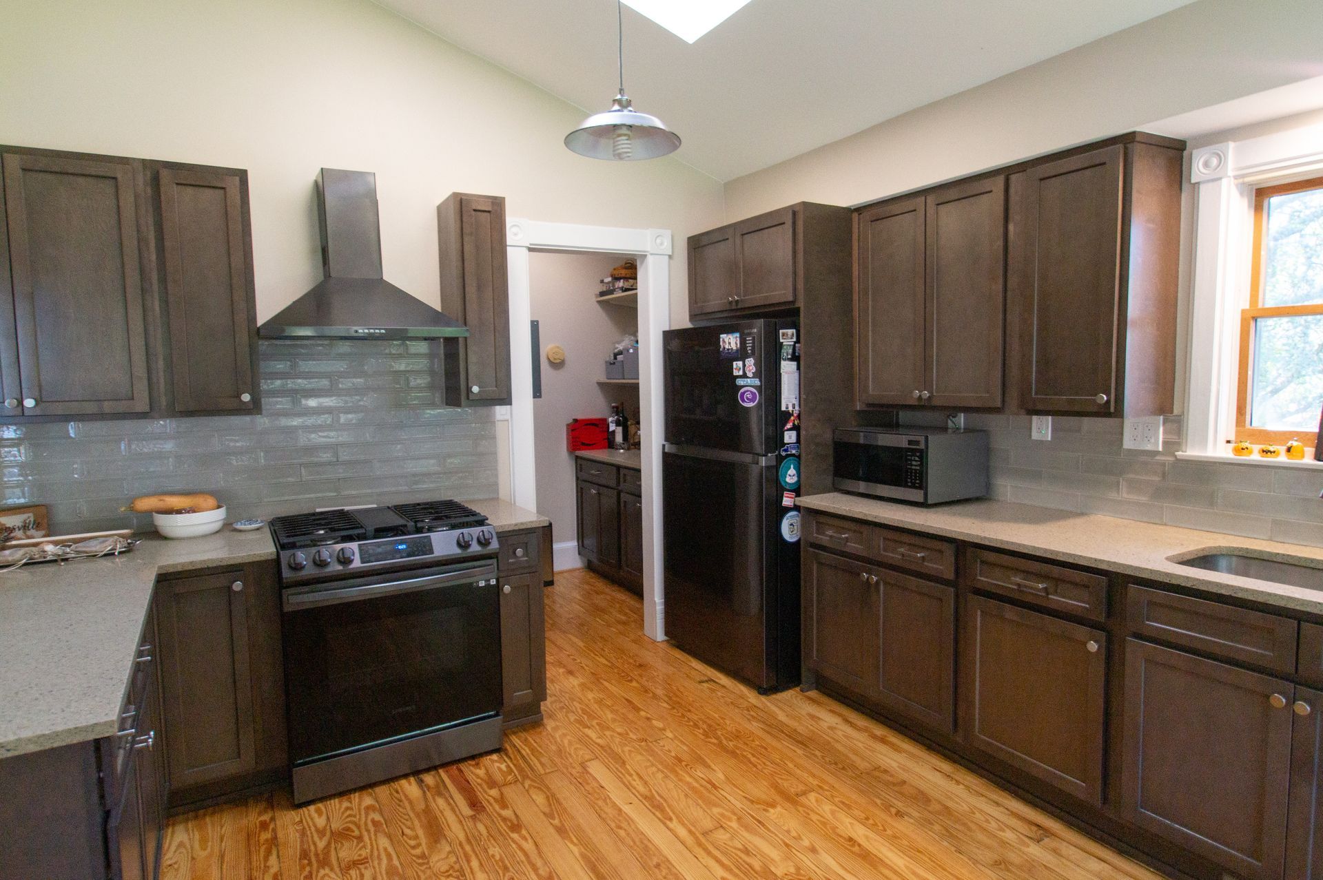 Kitchen with brown cabinets, stainless steel appliances, and light-colored countertops. Hardwood floors and a pantry are visible.