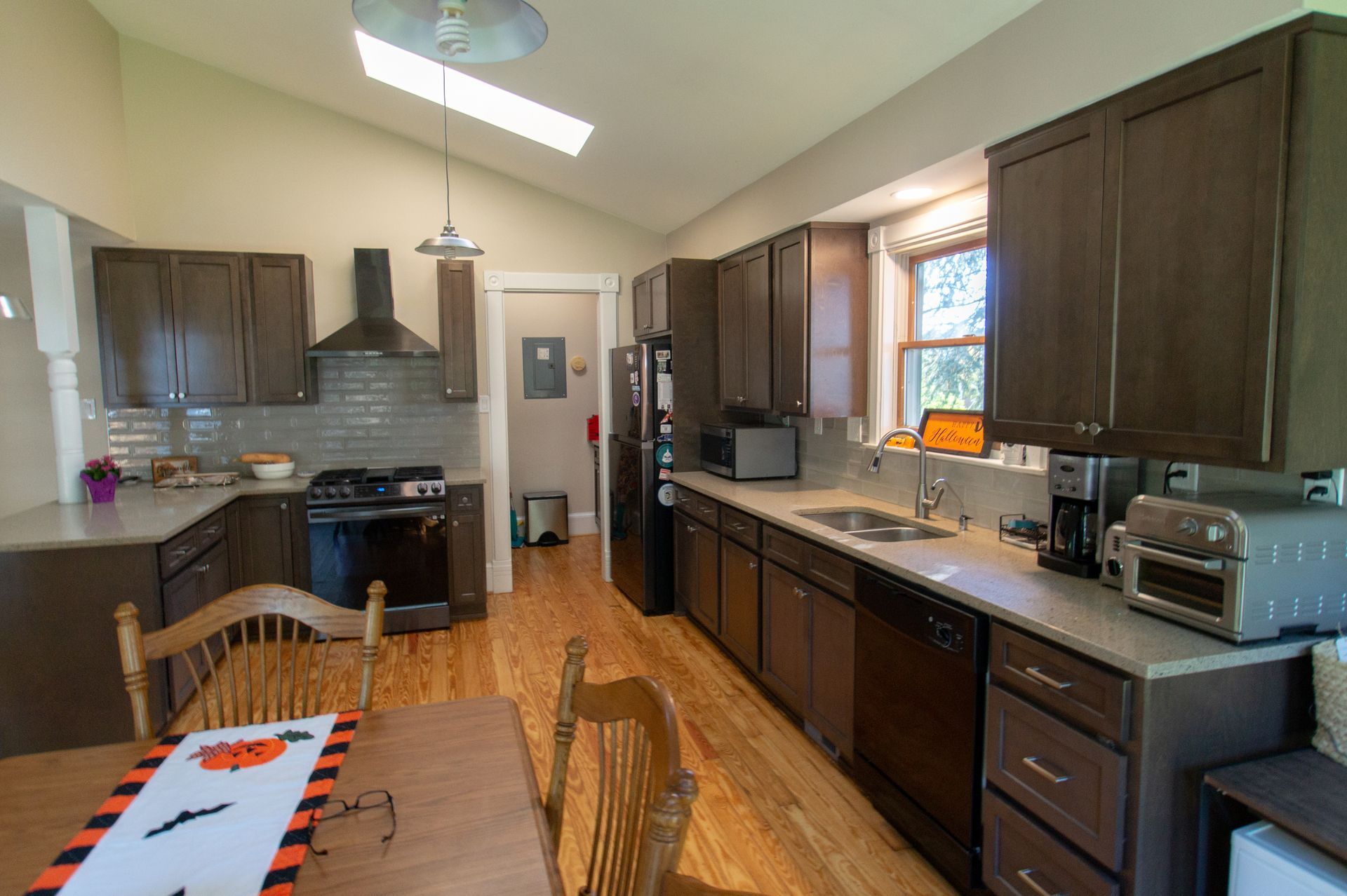 Kitchen with dark brown cabinets, light countertops, wood floor, and a black stove. Table with Halloween decor in the foreground.
