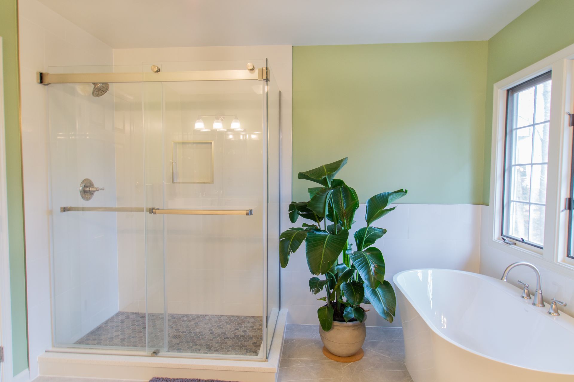Bathroom with a walk-in shower, freestanding tub, and a potted plant. Green and white walls, bright and airy.